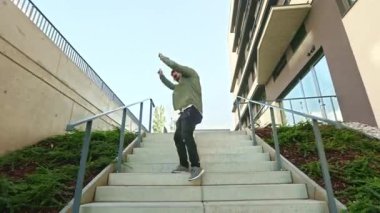 Merdivenlerden inip dans eden şık bir adamın yan görüntüsü. Sakallı yakışıklı erkek kulaklıkla müzik dinliyor, eğleniyor, gülümsüyor. Modern şehir hayatı kavramı.