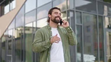 Sokaklarda dikilen, akıllı telefon kullanan, konuşan işadamlarının yan görüntüsü. Sakallı yakışıklı adam gülümsüyor, şaka yapıyor, dışarıda gülüyor. İş ve modern yaşam tarzı kavramı.