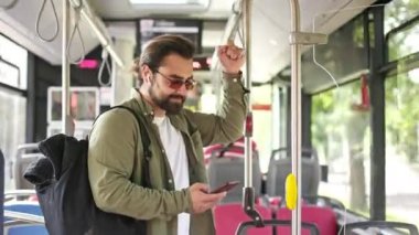 Yakışıklı bir adamın yanından geçerken, ayakta dururken, tutarken, akıllı telefon kullanırken. Esmer erkek, kulaklıklı, güneş gözlüklü, mesaj atan, kaydıran. Toplu taşıma kavramı.