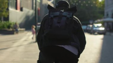 Sırt çantalı, şapkalı, şehirde bisiklet süren bir adam. Gündelik kıyafetler giyen genç bir erkek, şehirde yaz akşamının tadını çıkarıyor. Modern şehir yaşam tarzı kavramı.