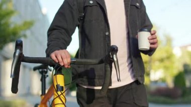 Sıradan kıyafetler giyen, bisikletle yürüyen, kahve içen bir adama yaklaş. Erkek, güneşli yaz havasında açık havada bisiklet sürüyor. Modern şehir yaşam tarzı kavramı.