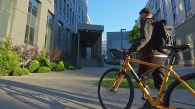 Erkek kurye, bisikletli teslimatçı. Sakallı, şapkalı ve sırt çantalı bir adam yazın şehir ortamında bisiklet sürüyor. Kentsel yaşam tarzı kavramı.