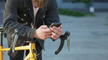 Sarı bisikletli bir adam şehrin dışında dikiliyordu. Esmer erkek, sakallı, akıllı telefon kullanıyor, okuyor, kaydırıyor, mesaj yazıyor. Kentsel yaşam kavramı.