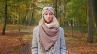 Front view of pretty, young lady walking in park, wearing stylish clothes. Beautiful, blonde woman standing, looking at camera, thinking, admiring. Concept of autumn and fall.