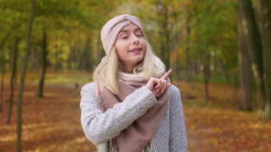 Front view of angry, strict woman standing in park, looking at camera. Attractive, blonde female wearing stylish clothes, telling, showing no, forbidding. Concept of autumn.