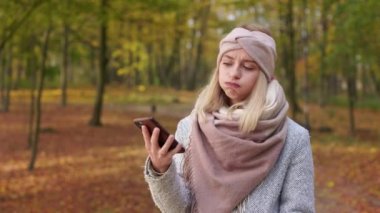 Side view of young lady using smartphone, pressing button, angry, irritated. Attractive, young woman wearing casual clothes, walking in park. Concept of modern lifestyle.