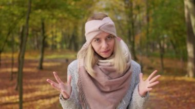 Front view of angry, irritated woman standing in park, looking at camera. Beautiful, blonde female calming down, closing eyes, walking, upset. Concept of autumn and fall.