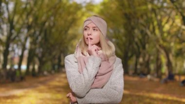 Front view of young, blonde woman walking in park in autumn. Beautiful lady standing, looking up, at camera, admiring, dreaming, thinking, smiling. Concept of autumn and fall.