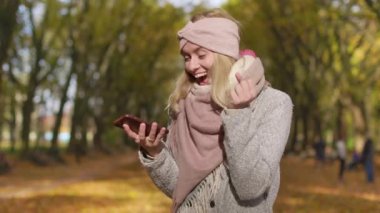 Side view of glad, surprised, happy girl jumping, showing hurray. Attractive, young woman using smartphone in park, smiling, texting. Concept of happiness and sincere emotions.