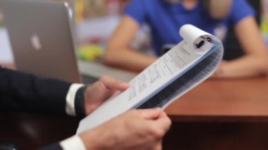 Close up of business partners sitting at table in office. Businessman wearing black costume, reading contract, partners making agreement. Concept of business and paperwork.