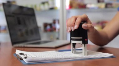 Close up of secretary, businesswoman putting stamp, seal on document, agreement. Young woman, female with manicure working in office at laptop. Concept of paperwork and business.