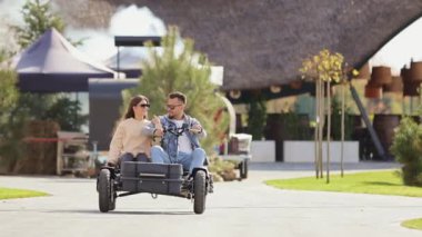 Front view of young couple driving buggy, looking at each other, hugging. Beloved man and woman having holiday, vacation, spending time together at resort. Concept of active rest.