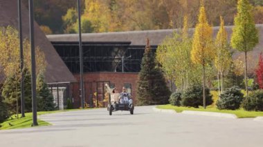 Front view of young, carefree woman and man driving buggy at resort. Beloved couple wearing sunglasses spending time together at nature in sunny weather. Concept of active rest.