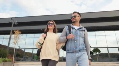 Front view of carefree couple having rest, recreation together. Two young people, boy and girl wearing sunglasses walking, holding by hands, smiling. Concept of happiness.