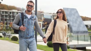 Front view of happy couple traveling together, walking at resort. Young people holding each other by hands, admiring nature, landscape, smiling. Concept of recreation and holiday.