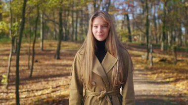 Zarif görünümlü, şık kıyafetler giyen, parkta yürüyen genç bir bayan. Çekici bir kadın ayakta, kameraya bakıyor, gülümsüyor. Güzellik kavramı ve doğa ile uyum.