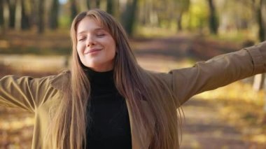 Sonbaharda parkta yürüyen mutlu bayanın yan görüntüsü. Güzel bir kadın şık kıyafetler giyiyor, doğanın tadını çıkarıyor, gözlerini kapıyor, gülümsüyor. Samimi duygular kavramı.
