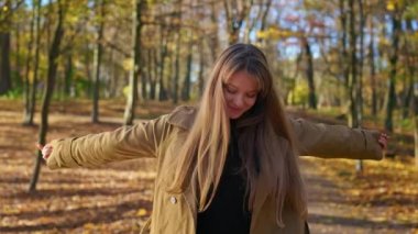 Front view of stylish woman wearing fashionable clothes, enjoying sunny autumn weather. Beautiful lady smiling, stretching hands, admiring, smiling. Concept of beauty of nature.