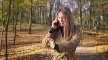 Side view of angry, upset, irritated woman standing in park, talking on phone. Fashionable, young female walking in park, quarreling, crying. Concept of urban lifestyle.