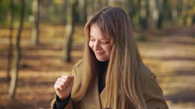 Front view of attractive woman walking in park, dancing with closed eyes. Cheerful lady wearing fashionable clothes, listening to music, smiling. Concept of modern lifestyle.