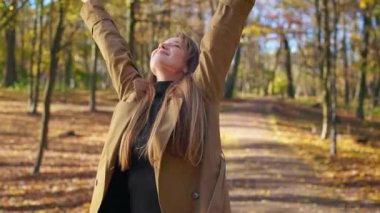 Front view of attractive, young lady walking in park, enjoying beauty. Happy, cheerful woman standing, raising hands, smiling, admiring. Concept of harmony with nature.