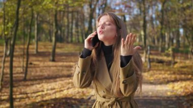 Side view of pretty, young female walking in park in autumn. Angry, irritated woman talking on phone, quarreling, crying, raising hands, standing. Concept of urban lifestyle.