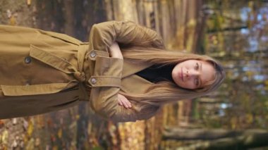 Front view of pretty, elegant lady wearing stylish clothes, walking in park. Happy, glad woman standing, looking at camera, crossing hands, smiling. Concept of modern lifestyle.