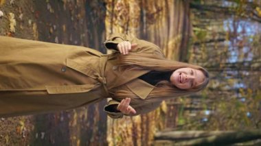 Front view of elegant, pretty female walking, standing in park in autumn. beautiful, young lady looking at camera, smiling, talking, explaining. Concept of happiness and enjoyment.