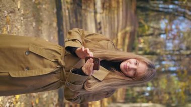 Front view of elegant, pretty lady wearing stylish clothes, walking in park. Cheerful, glad woman standing, using smartphone, smiling. Concept of happiness and harmony.