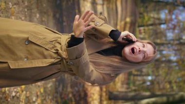Side view of pretty lady wearing fashionable clothes, walking, standing in park. Cheerful, glad woman talking on smartphone, telling, admiring. Concept of modern lifestyle.