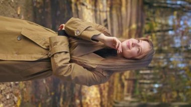 Side view of happy, glad lady standing in park, looking at camera. Beautiful, young woman leaning on hand, admiring, dreaming, smiling. Concept of harmony with nature.