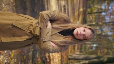 Front view of attractive, young lady walking in beautiful park, standing. Beautiful woman looking at camera, crossing hands, suspicious, concentrated. Concept of modern lifestyle.