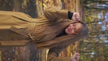 Front view of beautiful woman wearing elegant clothes, walking in park in autumn. Cheerful, smiling woman dancing, looking at camera, enjoying. Concept of happiness and joy.