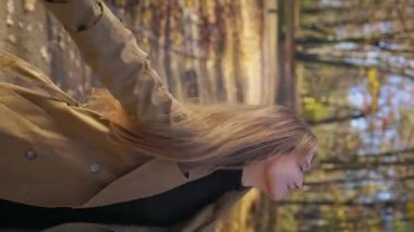 Side view of attractive lady wearing fashionable clothes, walking in park. Beautiful, young female closing eyes, turning, raising hands, enjoying. Concept of harmony with nature.
