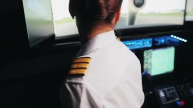 Uçağın kabininde oturan genç ve bayan pilotun arka görüntüsü. Üniformalı bir kadın. Tutuyor, dönüyor, direksiyona geçiyor, bakıyor. Havacılıkla seyahat kavramı.