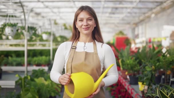 吸引人的 年轻的花匠 喜欢在温室里工作 华丽的前景色 积极的女士拿着水壶 露出微笑 幸福与欢乐的概念 — 图库视频影像