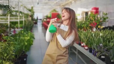 Neşeli, pozitif kadın üniforması giyiyor, işten zevk alıyor. Mutlu, güzel çiçekçi üniforma giyiyor, bitkileri ilaçlıyor, şarkı söylüyor. Mutluluk ve keyif kavramı.