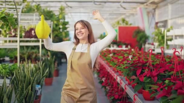 正のフロントビューでは 陽気な女性の制服を着て オレンジ 温室で働いている 美しい女性の保持鍋 散水植物 幸せと誠実な感情の概念 — ストック動画