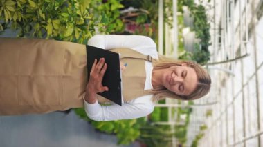 Neşeli, pozitif bayanın ayakta durması, seradaki bitkilerle ilgilenmesi. Önlük giyen, not alan güzel, genç bir çiçekçi. Sera ve portakallık kavramı.