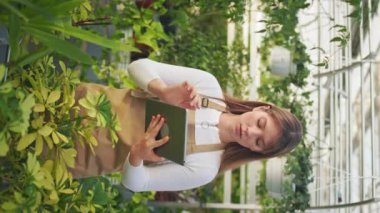 Çekici kadın çiçekçinin büyümesi, bitkilerle ilgilenmesi. Güzel, genç bir bayan tablet kullanıyor, bakıyor. Bitkileri saymak. Modern şehir yaşam tarzı kavramı.