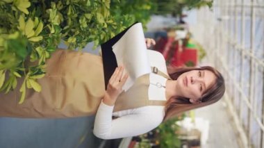 Kadın çiçekçinin büyüdüğünü, seradaki bitkilerle ilgilendiğini gördüm. Çekici, genç bayan ayakta, klasörü tutuyor, yazıyor, düşünüyor. Modern, kentsel yaşam tarzı kavramı.