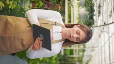 Serada çalışan çekici genç bir bayanın yan görünüşü, portakalcılık. Güzel bayan çiçekçi ayakta, elinde tablet, düşünüyor, not alıyor. İşten zevk alma kavramı.