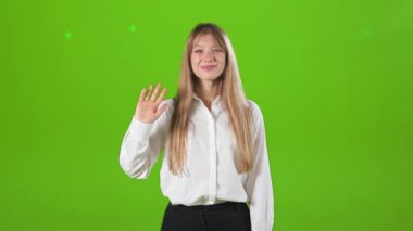 Dost canlısı, neşeli bir bayanın stüdyoda kameraya bakıp el sallamasının ön görüntüsü. Çekici, genç bir kadın elini kaldırıyor, selamlıyor. Mutluluk kavramı ve samimi duygular.