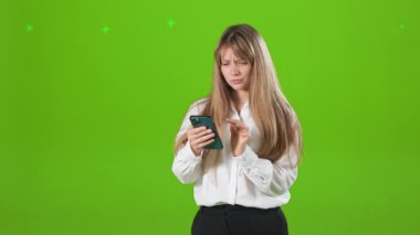 Akıllı telefondan çalışan, daktilo eden, kaydıran genç ve güzel bir bayanın yan görüntüsü. Güzel, sarışın kadın resmi kıyafetler giyiyor, düşünüyor. Yeşil stüdyo arka planında izole edilmiş..