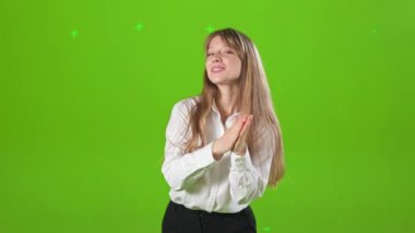 Stüdyoda elini uzatıp alkışlayan neşeli genç bir bayanın ön görüntüsü. Güzel, sarışın kadın kameraya bakıyor, gülümsüyor. Yeşil stüdyo arka planında izole edilmiş..