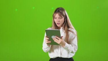 Stüdyoda duran, elinde tablet tutan, kullanan, okuyan sarışın genç bir kadının yan görüntüsü. Çekici, sarışın kadın tablet kullanıyor, hurra gösteriyor. Modern teknoloji kavramı.