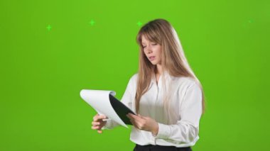 Çalışkan bir kadının stüdyoda, kapalı alanda çalışmasının yan görüntüsü. Genç, sarışın bir kadın klasörü tutuyor, okuyor, odaklanmış, odaklanmış. Yeşil stüdyo arka planında izole edilmiş..