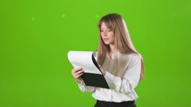 Genç, sarışın bayan, iş kadını klasörü tutuyor, kitap okuyor. Resmi kıyafetler giyen güzel bir kadın, bilgileri inceliyor. Yeşil stüdyo arka planında izole edilmiş..