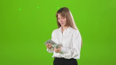 Başarılı ve zengin bir kadının stüdyoda durup para saymasının yan görüntüsü. Sarışın, güzel kadın resmi kıyafetler giyiyor. Yeşil stüdyo arka planında izole edilmiş..