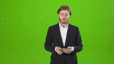 Önde kostüm giyen, elinde para tutan, para sayan genç iş adamları var. Kostüm ve gömlek giyen yakışıklı, başarılı bir adam. Yeşil stüdyo arka planında izole edilmiş.,